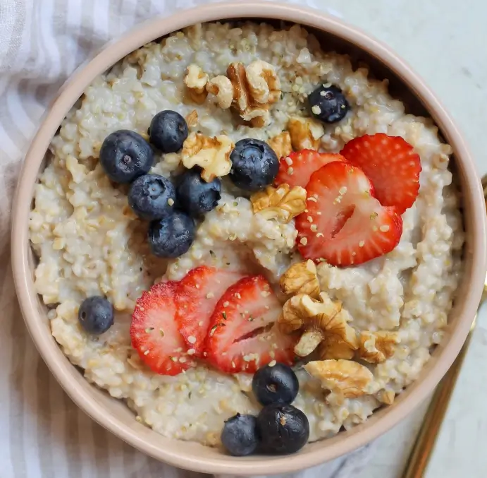 Overnight steel cut oats topped with fresh strawberries, blueberries, and walnuts in a beige bowl.