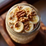 Banana muffin overnight oats in a mason jar topped with bananas