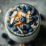 blueberry paleo oats in a glass jar topped with coconut and blueberries